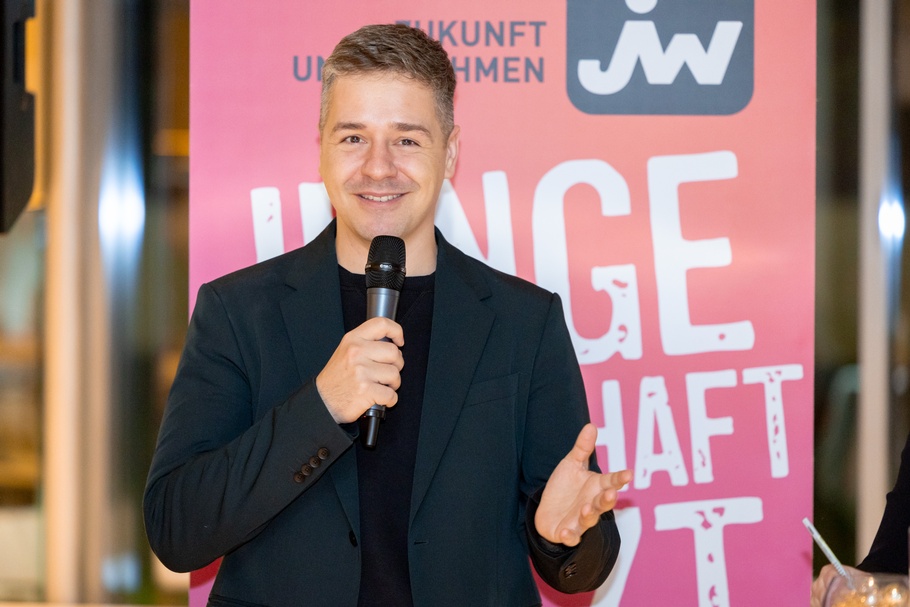 Zu sehen ist eine Person bei einer Veranstaltung, die in ein Mikrofon spricht.