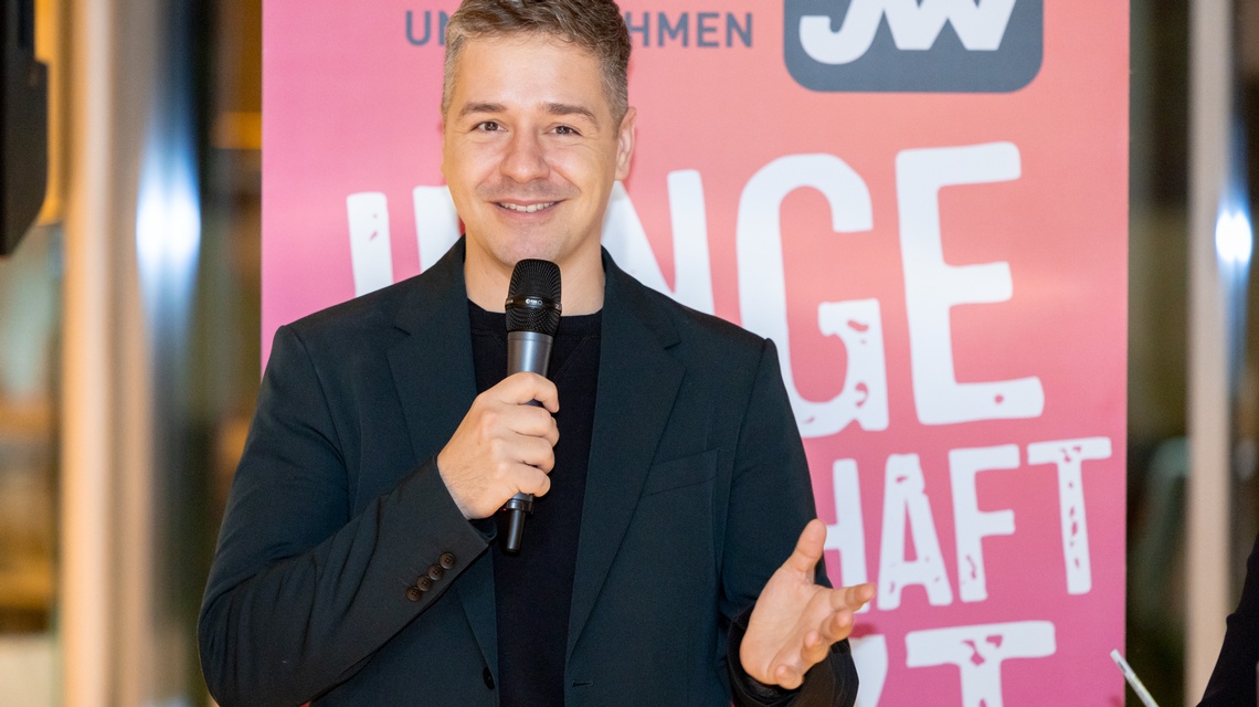 Zu sehen ist eine Person bei einer Veranstaltung, die in ein Mikrofon spricht.