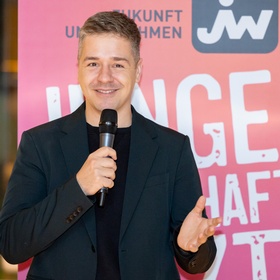 Zu sehen ist eine Person bei einer Veranstaltung, die in ein Mikrofon spricht.