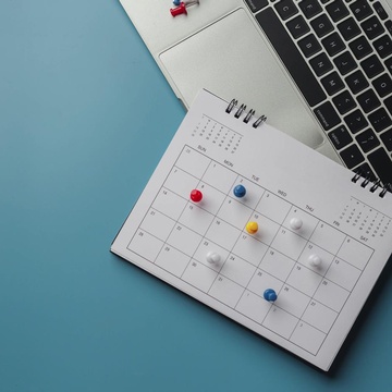 Kalender mit Pin-Nadeln liegt auf einem Laptop, Vogelperspektive