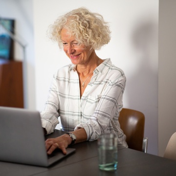 Lächelnde Person sitzt an Tisch und blickt auf Laptop
