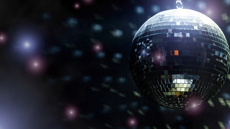 Eine Discokugel hängt von der Decke eines dunklen Partyraums, In der Disco sieht man Konfetti und die Reflektionen der Discokugel, die eine Lichtstimmung erzeugen. 